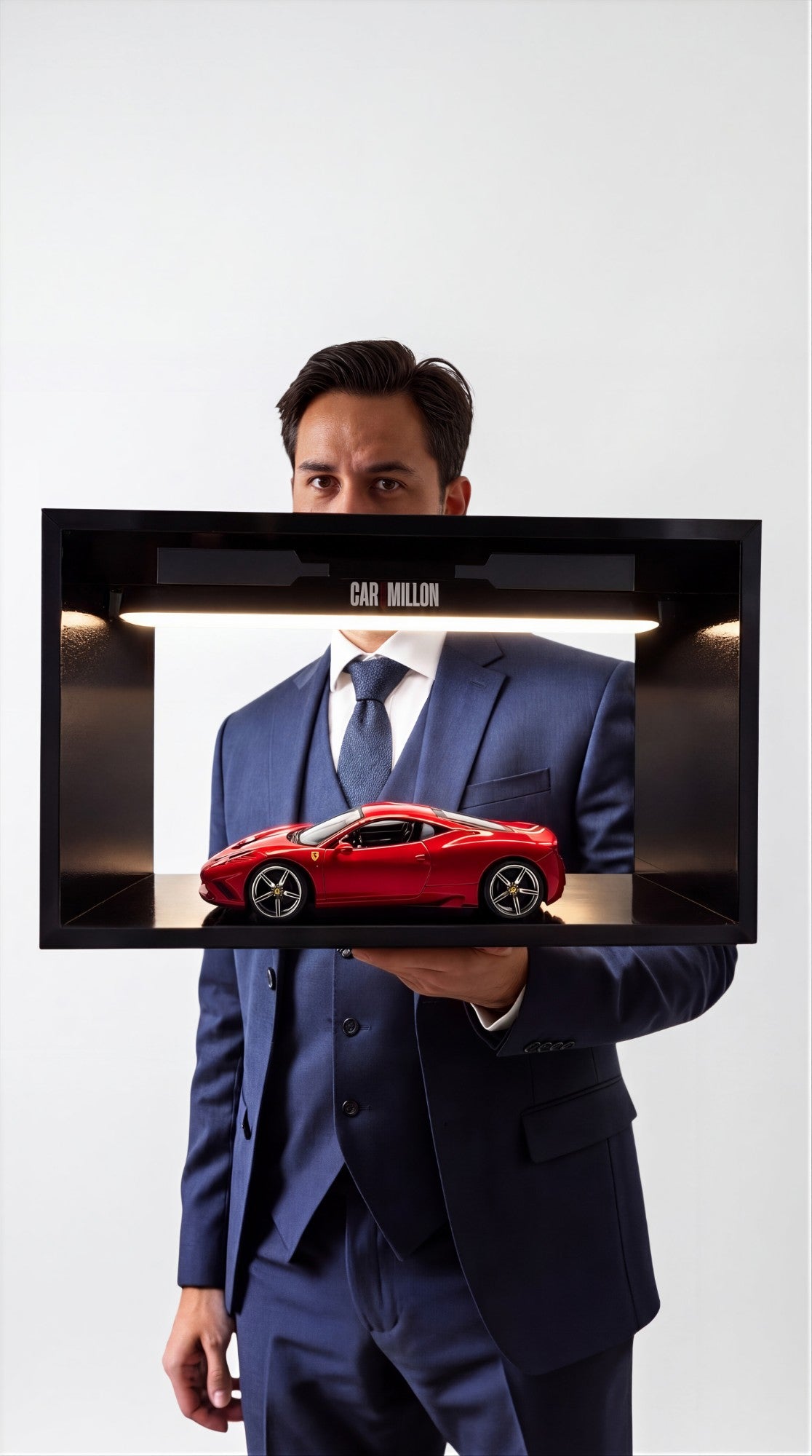 A collector in a navy three-piece suit holding his CAR1MILLON composition, a red Ferrari lit beneath the light bar